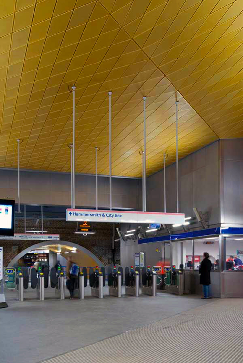 Anodised gold aluminium ceiling and shot-peened stainless steel cladding to ticket hall. Wood Lane underground station for London, Underground in partnership with Westfield - Architectural metalworks, platform seating, Double Stone Steel Europe Ltd. - Main contractor: Costain - Architect: Ian Ritchie architects - Principal engineer: Waterman Civils