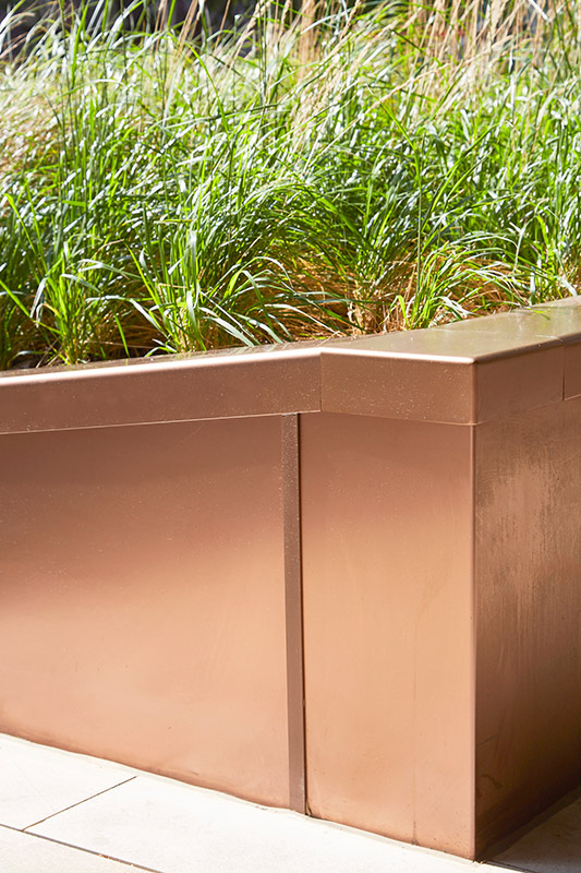 PVD coloured stainless steel in sandblasted Bronze, corner section of planter. In sunlight the Bronze PVD has a rich depth. Embassy Gardens, London, UK PVD coloured stainless steel in sandblasted Bronze, corner section of planter. In sunlight the Bronze PVD has a rich depth. Embassy Gardens, London, UK