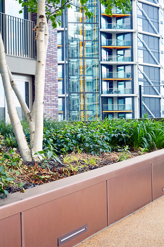 PVD coloured stainless steel in sandblasted Bronze which was specified to complement the green planting . Embassy Gardens, London, UK. PVD coloured stainless steel in sandblasted Bronze which was specified to complement the green planting . Embassy Gardens, London, UK.