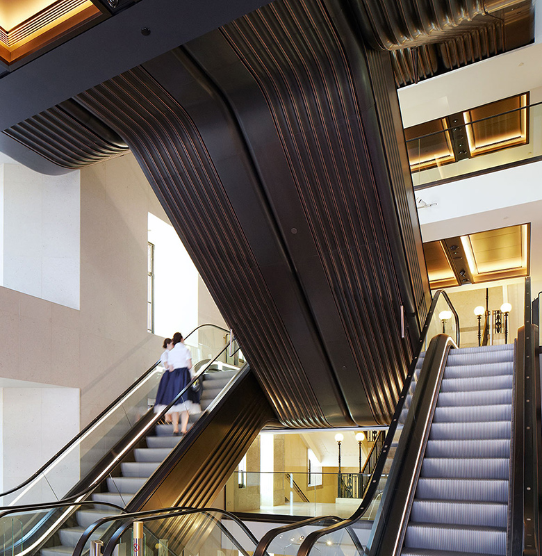 The escalators redolent of the Art Deco period. Architectural design by Make Architects. PVD coloured stainless steel trim by Double Stone Steel Europe Ltd. The escalators redolent of the Art Deco period. Architectural design by Make Architects. PVD coloured stainless steel trim by Double Stone Steel Europe Ltd.