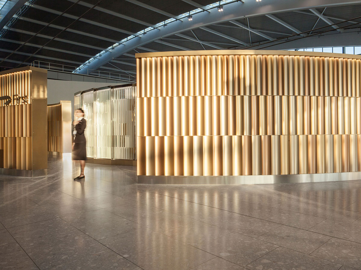 Undulating 3 metre high screen in Chocolate, Champagne and Almond Gold PVD coloured stainless steel forms entrance to British Airways Private Check-In, Heathrow Terminal 5, London.  - Architects/Interior Designers: Universal Design Studio - PVD Coloured Stainless Steel: Double Stone Steel Europe Ltd - Photography: Paul Greenleaf