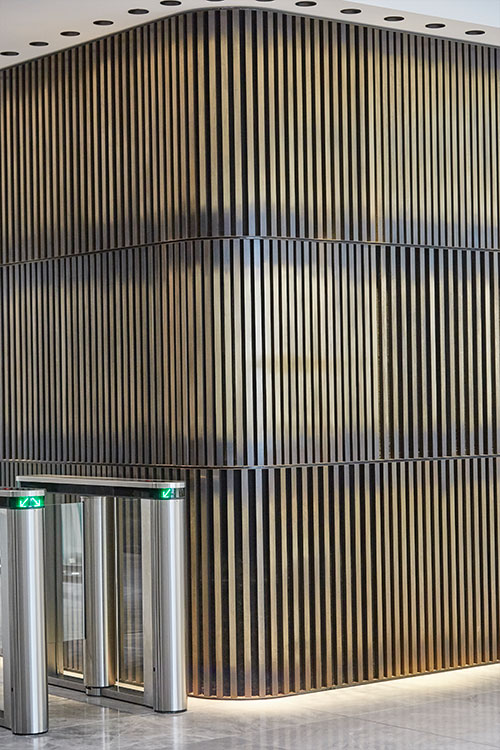 1 Broadgate Quarter, Snowden St, London, EC2A 2AW - Architects: John Robertson Architects. - Stainless Steel Canopy: Double Stone Steel Europe Ltd. - The rear wall clad in three rows of narrow brass bars creates a warm, welcoming backdrop to the reception area.