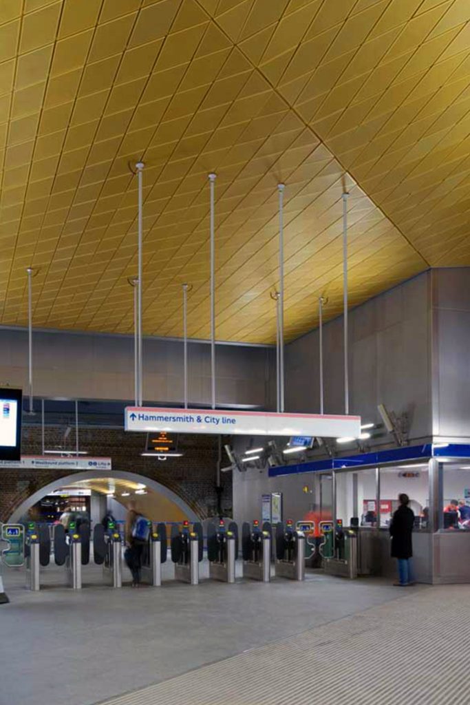 Showing the gold, or brass-coloured, anodised aluminium diagonally-set ceiling panels to the Wood Lane Underground Station, London. Architectural design by Ian Ritchie Architects. Ceiling by Double Stone Steel Europe Ltd.